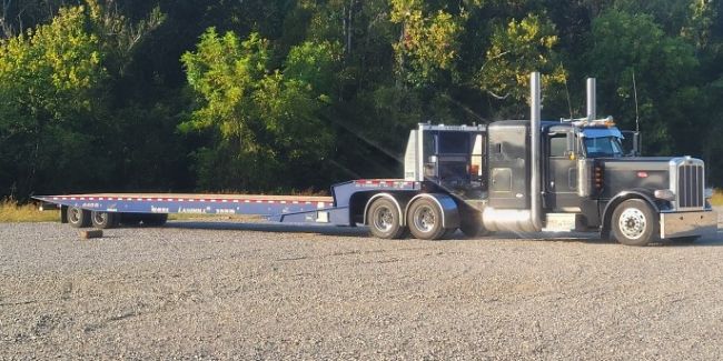 Long low flatbed trailer behind black semi truck with tall chrome exhausts
