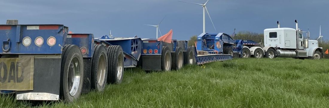 Long blue trailer on grass being pulled by a white semi truck